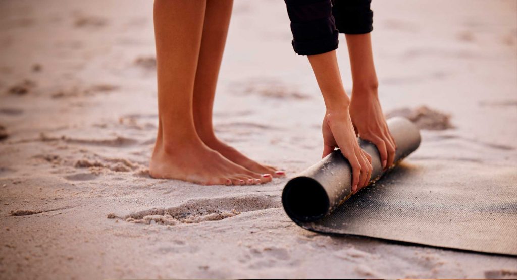 Imagen de una chica enrollando esterilla de yoga en la playa de la Costa Brava
