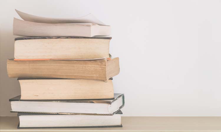 Pila de libros de yoga y filosofía espiritual apilados sobre una superficie neutra, símbolo de estudio, aprendizaje y profundización en la práctica del yoga