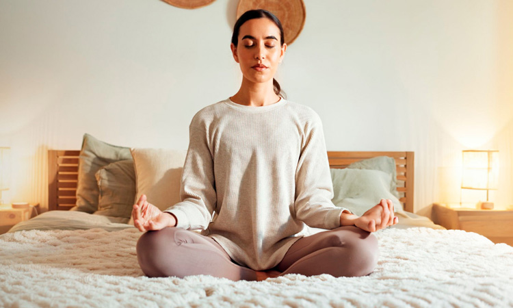Imagen de una mujer practicando meditación sobre la cama